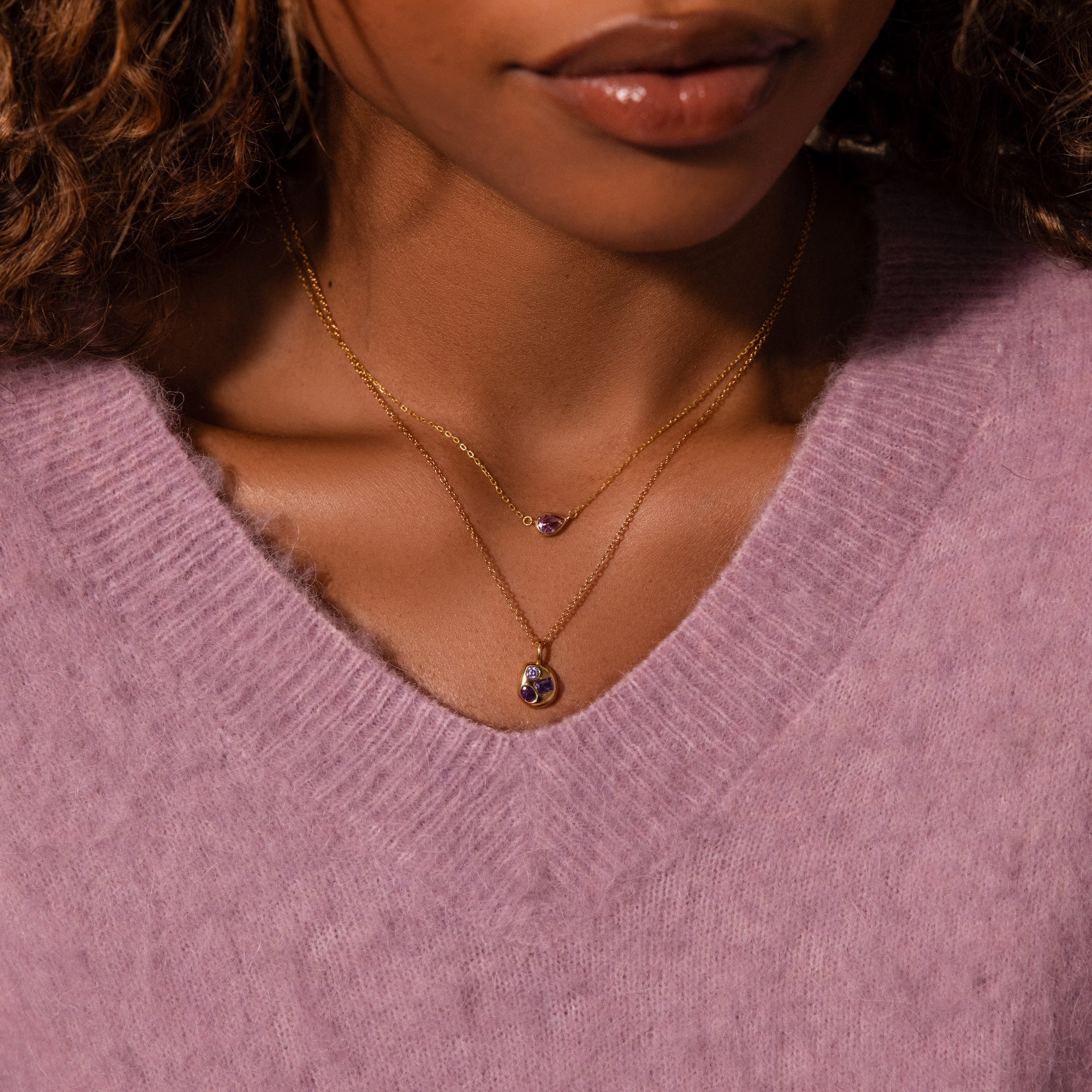 Woman wearing a lilac sweater and the Mixed Birthstone Capsule Necklace featuring two purple gemstone pendants.
