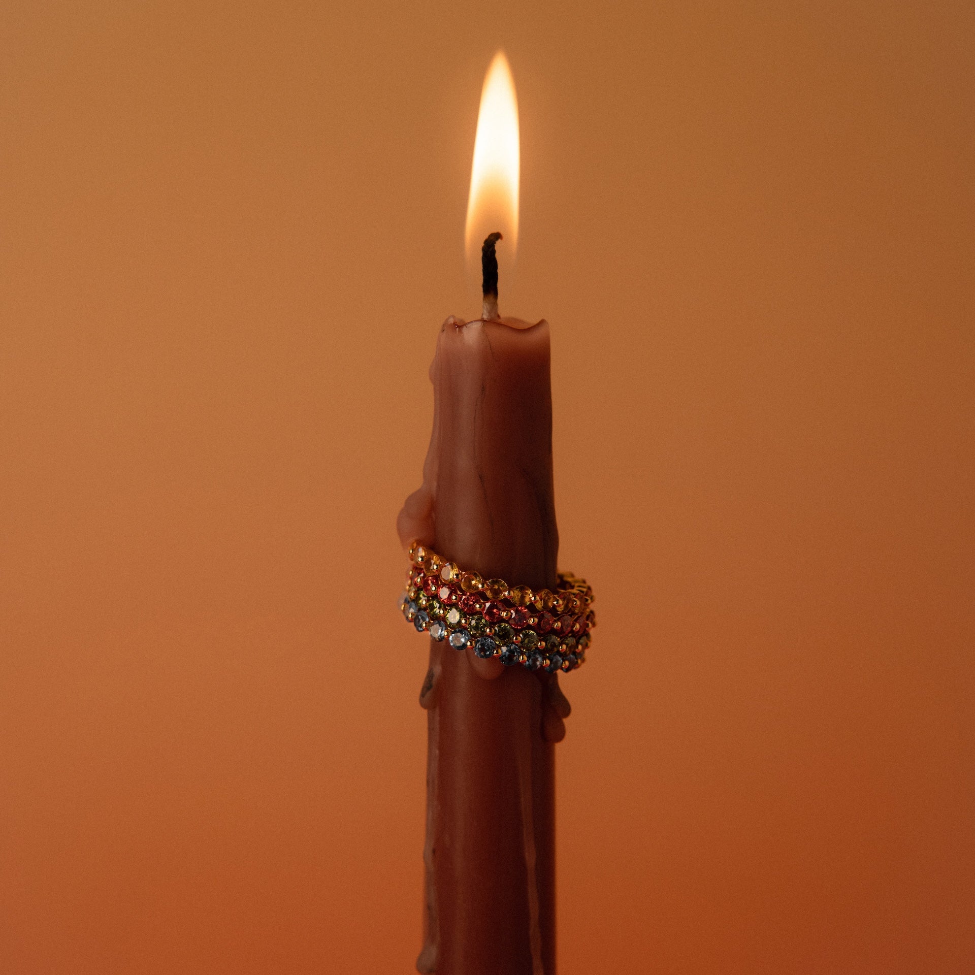 A lit brown candle adorned with three Lace Eternity Topaz Rings, set against a simple warm-toned background.