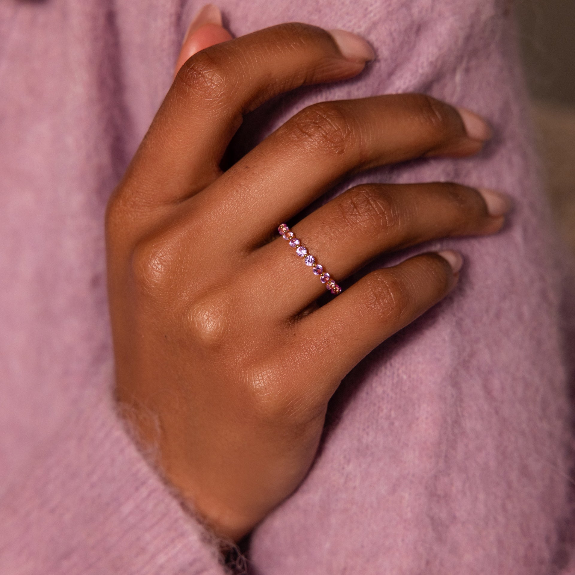 A hand wearing the Lace Eternity Pink Tourmaline Ring rests on a lavender sweater, highlighting the jewelry.