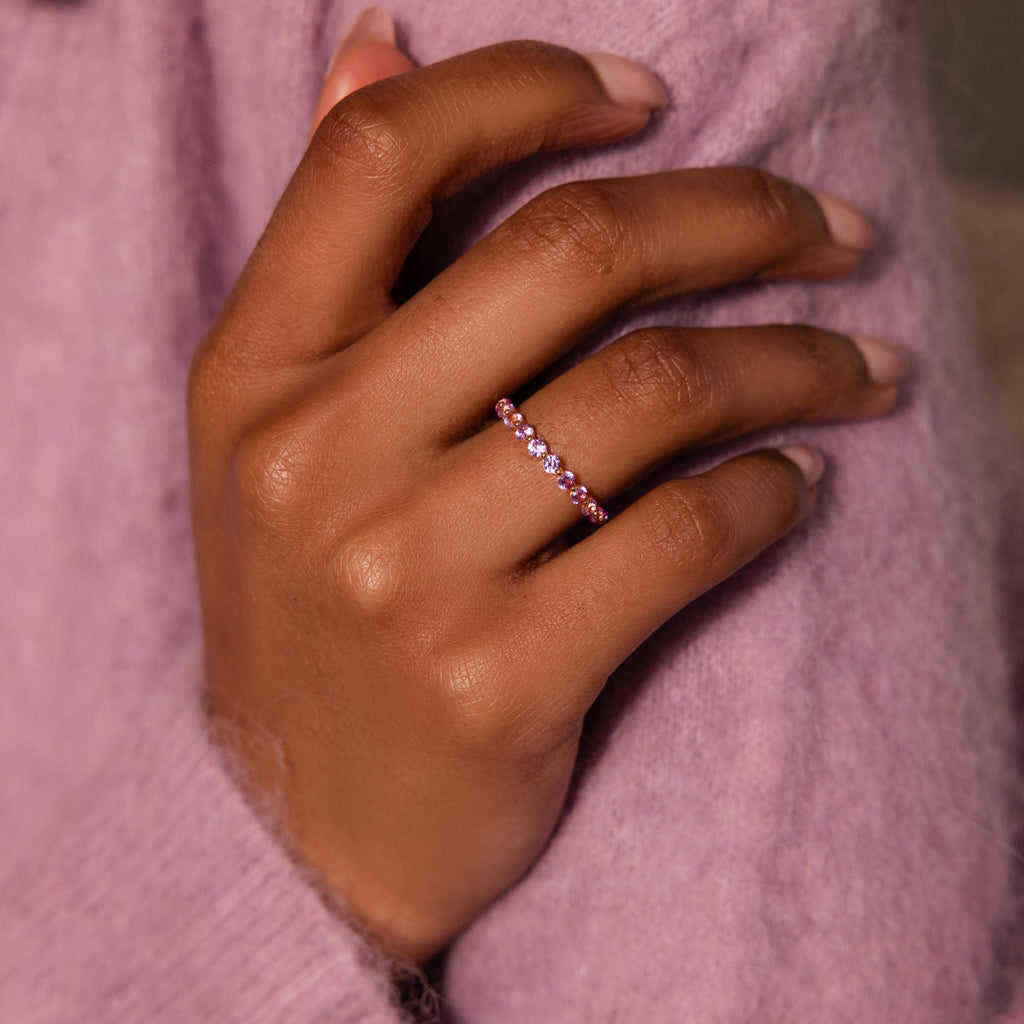 A hand wearing the Lace Eternity Emerald Ring rests on a lavender sweater with delicate lace accents.