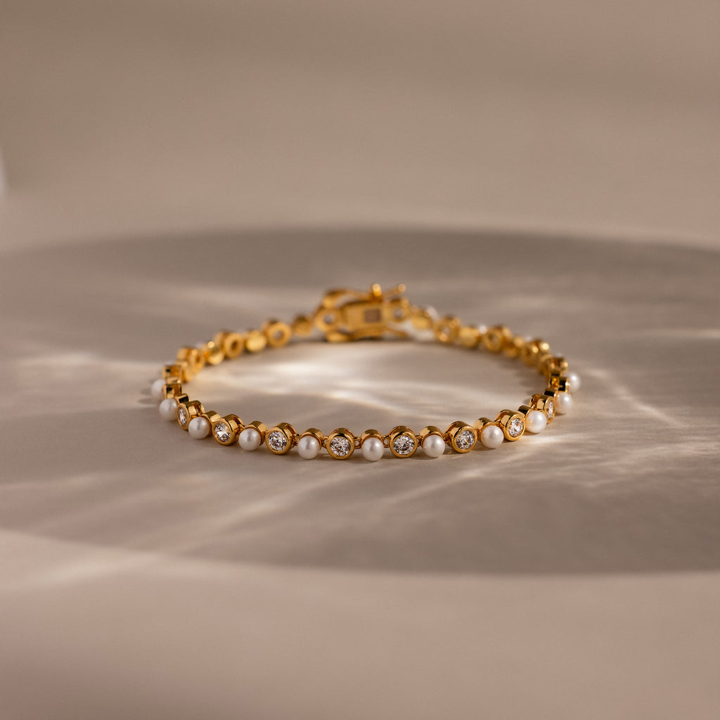 The Pearl & Diamond Tennis Bracelet features alternating pearls and diamonds in a luxurious gold design, elegantly displayed on a neutral background.