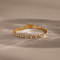 The Pearl & Diamond Tennis Bracelet features alternating pearls and diamonds in a luxurious gold design, elegantly displayed on a neutral background.