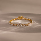 The Pearl & Diamond Tennis Bracelet features alternating pearls and diamonds in a luxurious gold design, elegantly displayed on a neutral background.