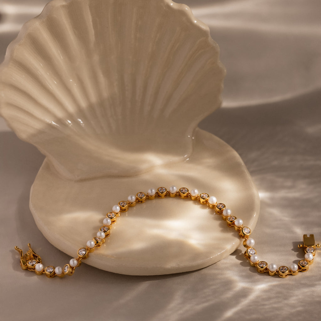 The Pearl & Diamond Tennis Bracelet, shown on a ceramic seashell dish in gentle natural light, is an elegant accent for any luxury jewelry collection.