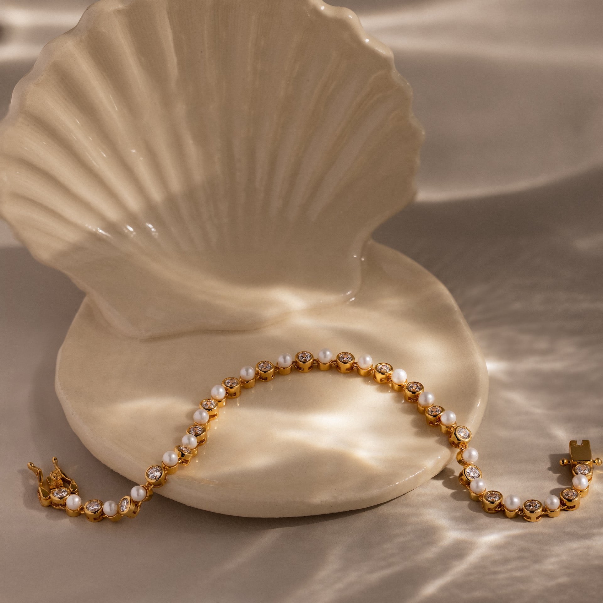 The Pearl & Diamond Tennis Bracelet, shown on a ceramic seashell dish in gentle natural light, is an elegant accent for any luxury jewelry collection.