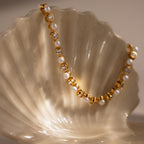 The Pearl & Diamond Tennis Bracelet is draped elegantly over a pearly white seashell, showcasing its luxurious blend of gold, pearls, and diamonds.