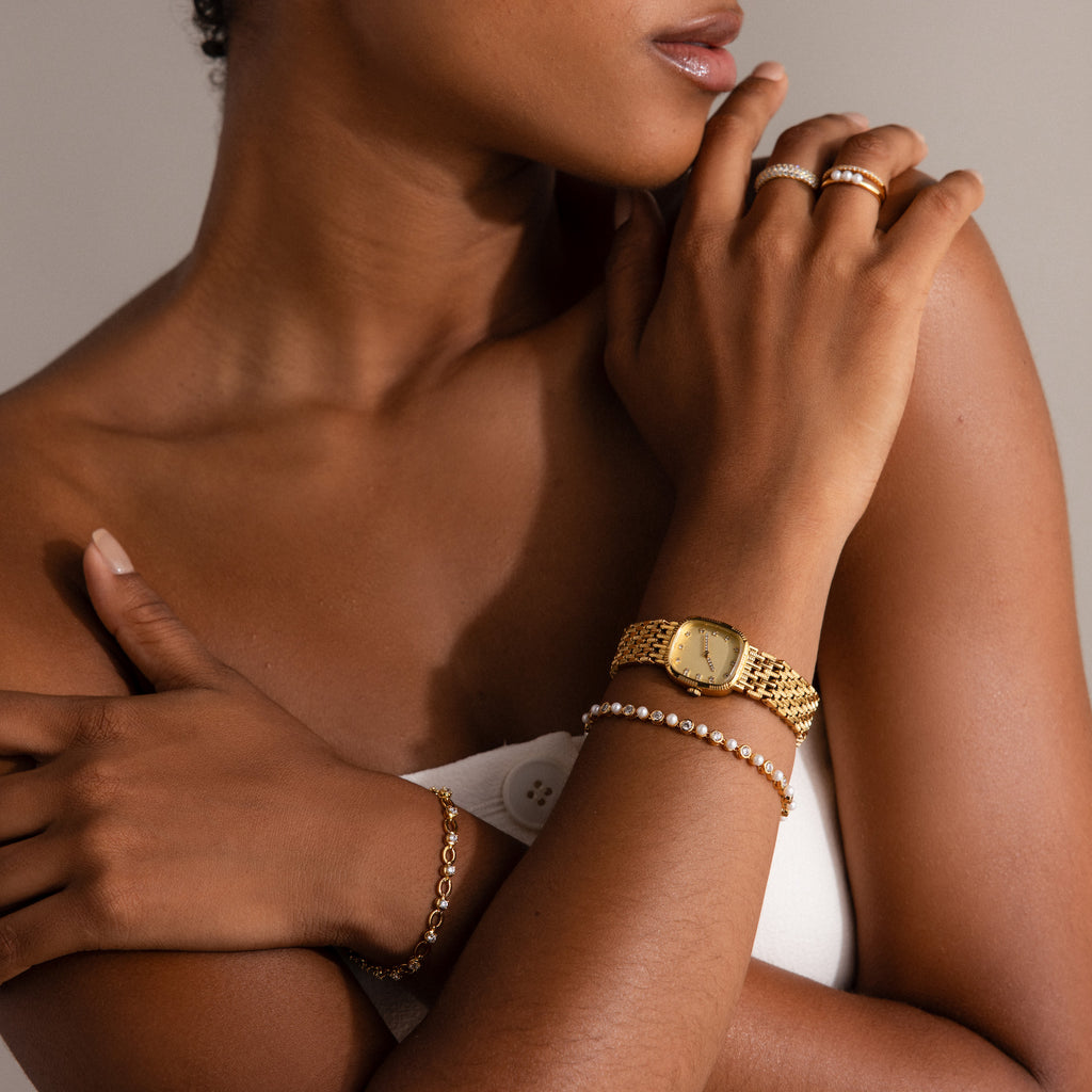 A woman poses with her hands near her face, showcasing gold jewelry and the Pearl & Diamond Tennis Bracelet.