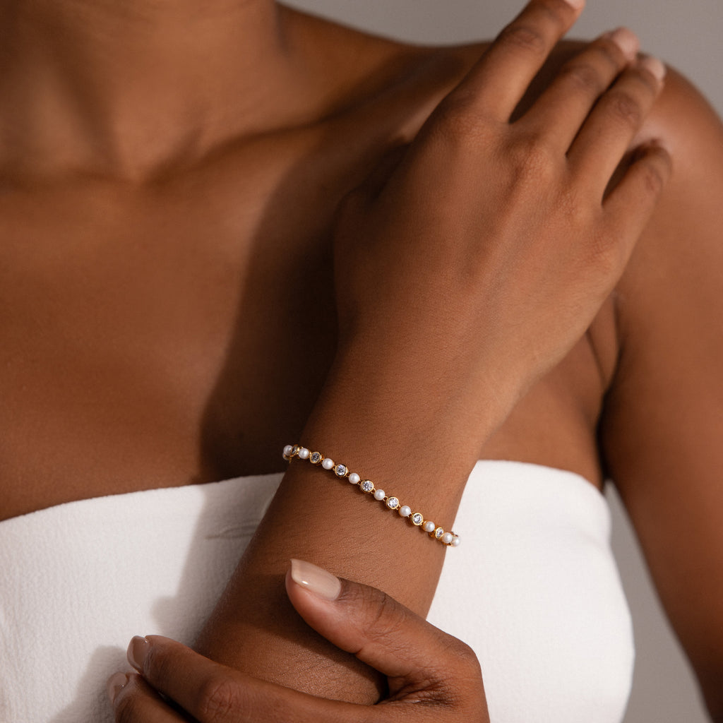 Woman in a white strapless top wearing the Pearl & Diamond Tennis Bracelet, a delicate luxury accessory featuring sparkling diamonds.