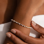 A close-up of the Pearl & Diamond Tennis Bracelet, adorned with pearls and diamonds, elegantly displayed on a wrist with gently touching hands.