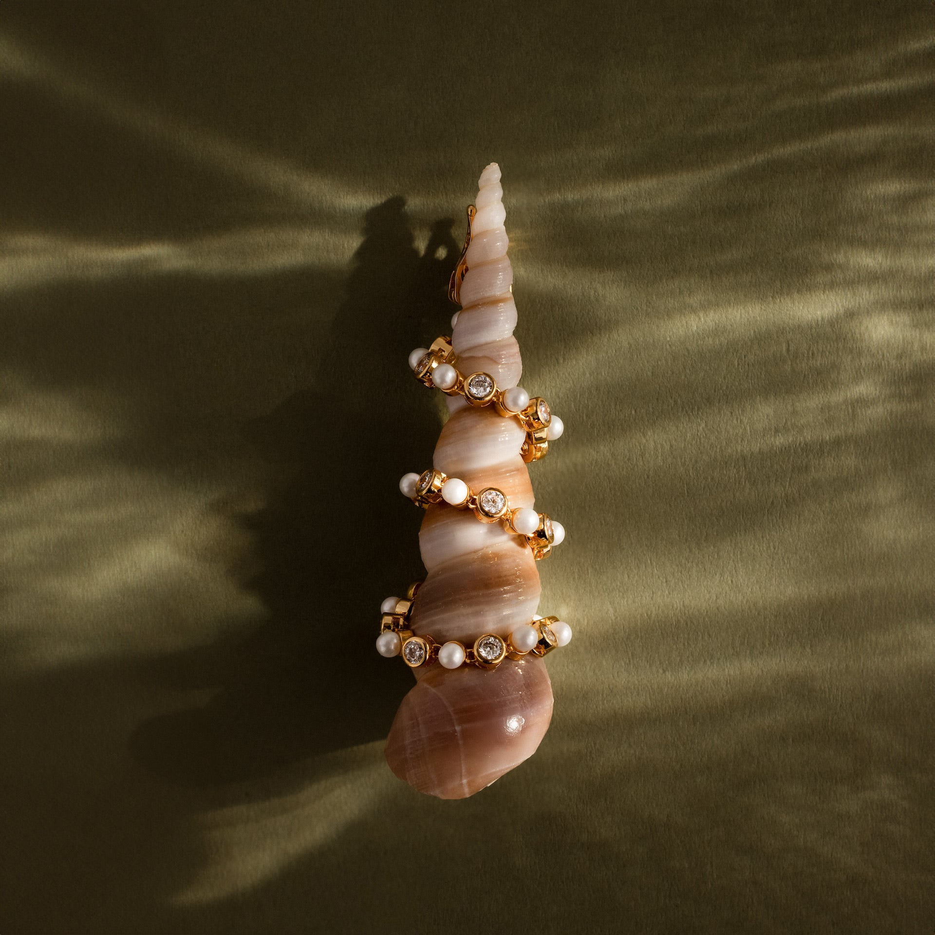 A Pearl & Diamond Tennis Bracelet, set against a textured olive-green background, evokes the refined elegance of luxury jewelry.