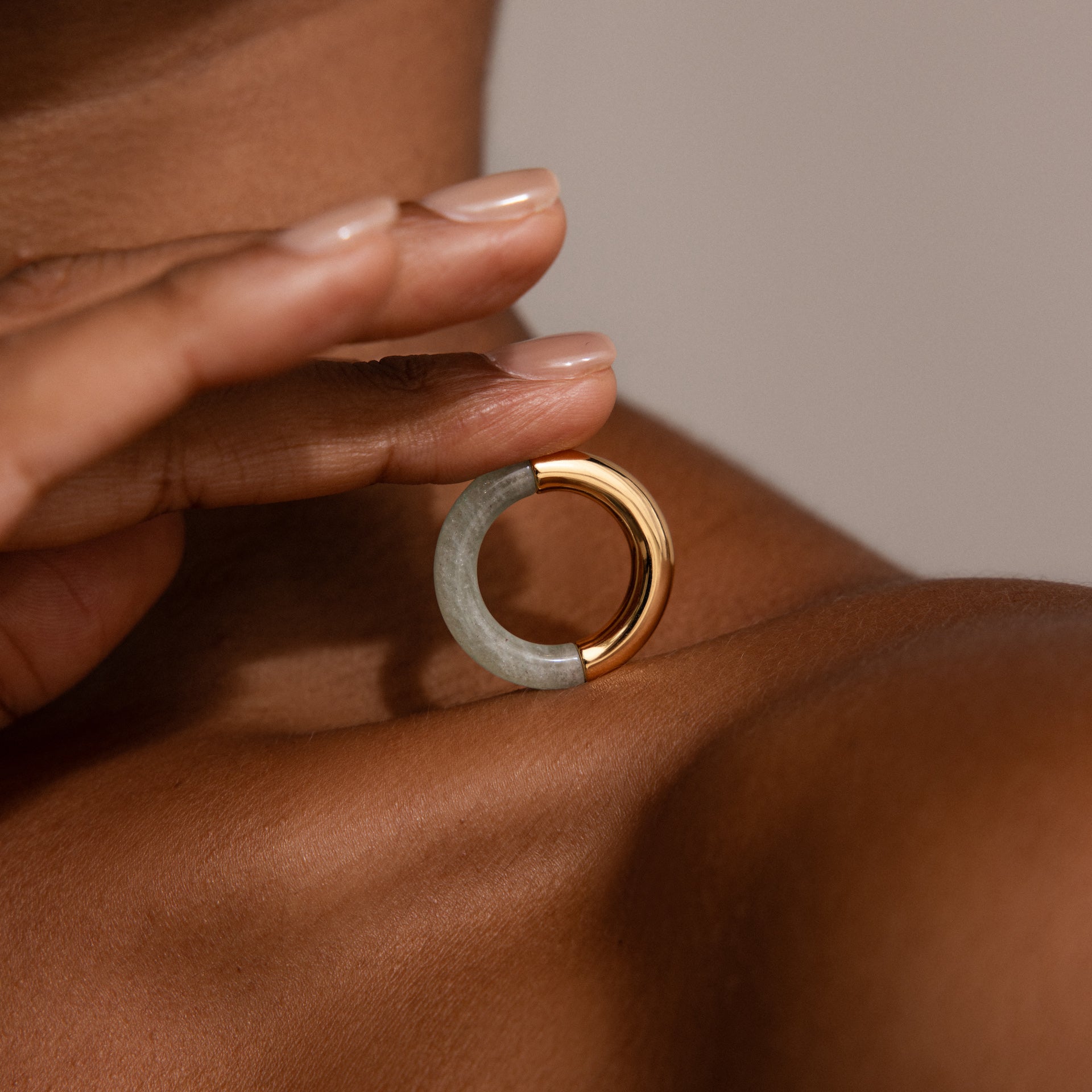A person holds the Half Jade Ring, a striking statement jewelry piece, on their shoulder.