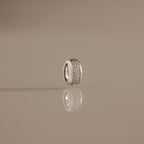 The Bold Pave Dome Charm in Silver, adorned with rows of sparkling stones and standing upright on a reflective beige surface, showcases timeless elegance in every detail.