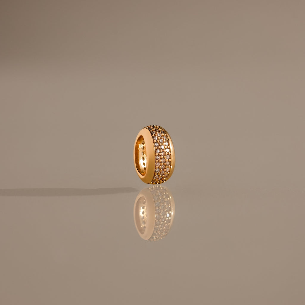 The Bold Pave Dome Charm in 18K Gold features rows of sparkling diamonds, elegantly displayed upright on a reflective, neutral surface for a sophisticated presentation.