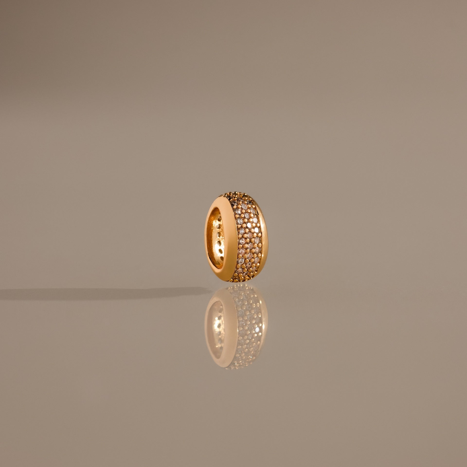 The Bold Pave Dome Charm in 18K Gold features rows of sparkling diamonds, elegantly displayed upright on a reflective, neutral surface for a sophisticated presentation.