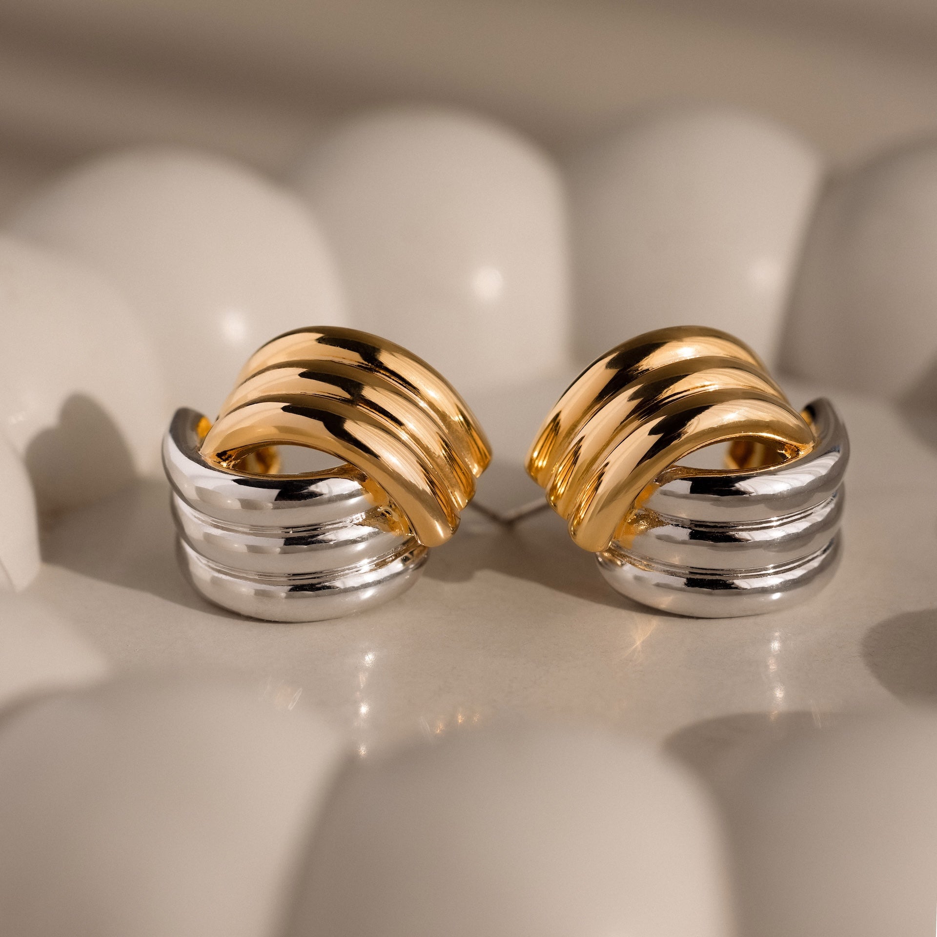 Ribbed Mixed Metal Studs featuring a twisted gold and silver design are displayed on a curved, light-colored surface.