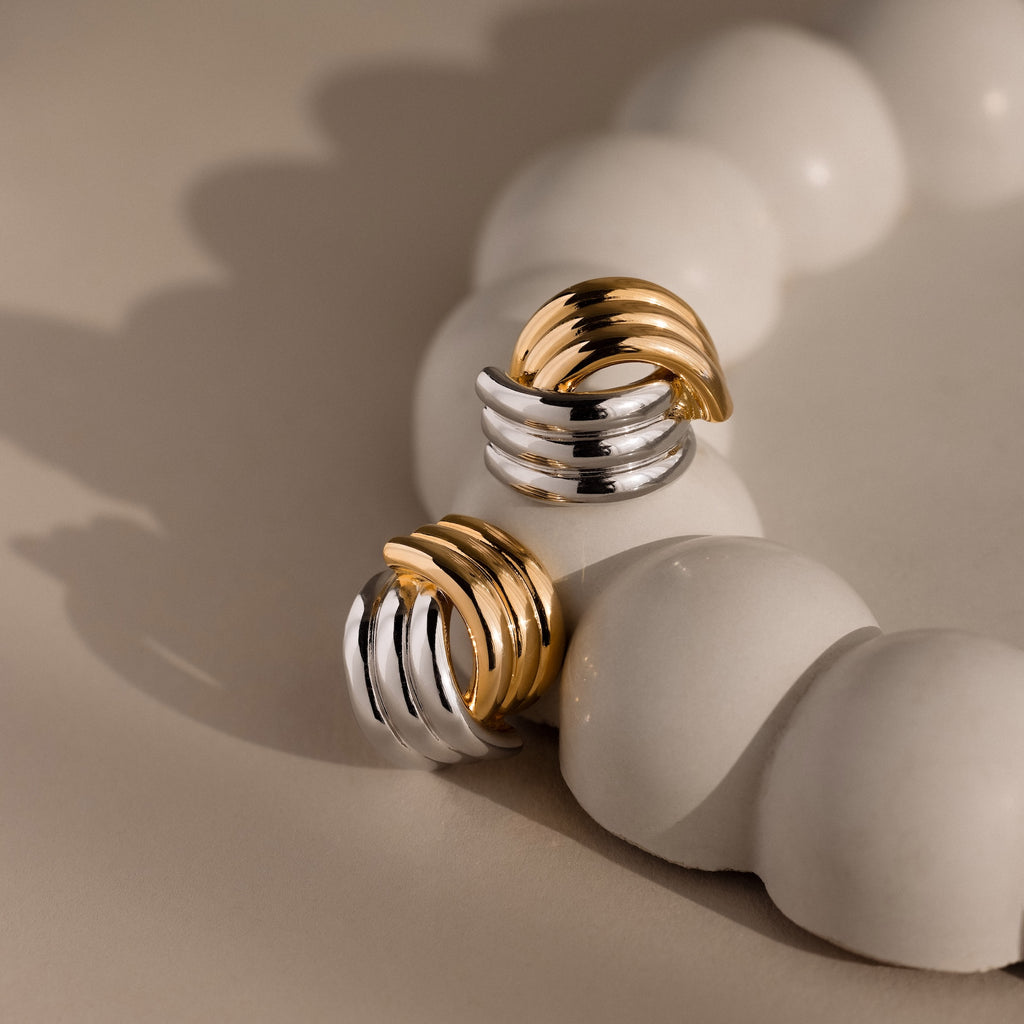 Ribbed Mixed Metal Studs, featuring gold and silver chunky hoops with sculpted ridges, showcased on a smooth white decorative surface.