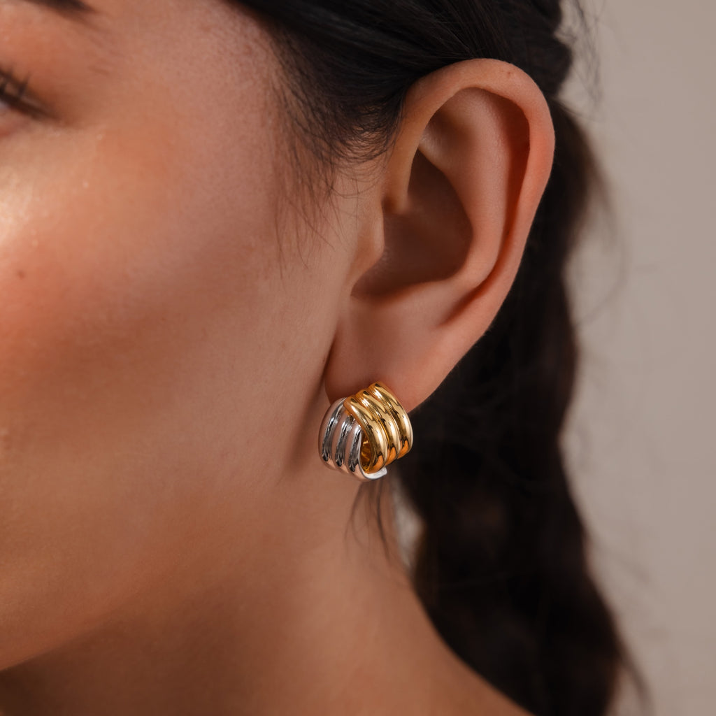 Close-up of a woman's ear adorned with Ribbed Mixed Metal Studs, featuring chunky gold and silver sculpted ridged hoops.