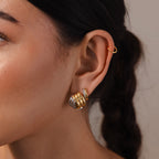 Close-up of a woman's ear adorned with Ribbed Mixed Metal Studs—sculpted ridged earrings in gold and silver for a modern look—plus a gold hoop cuff, her dark braided hair visible.