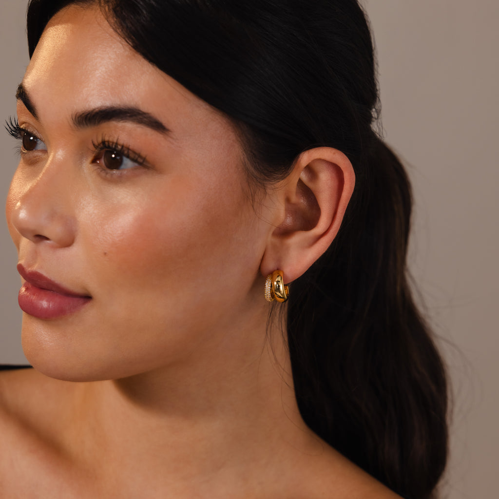 A woman with long dark hair wears the Duo Pave Dome Studs, gazing to the side with a neutral expression—these earrings add an elegant accent to her everyday look.