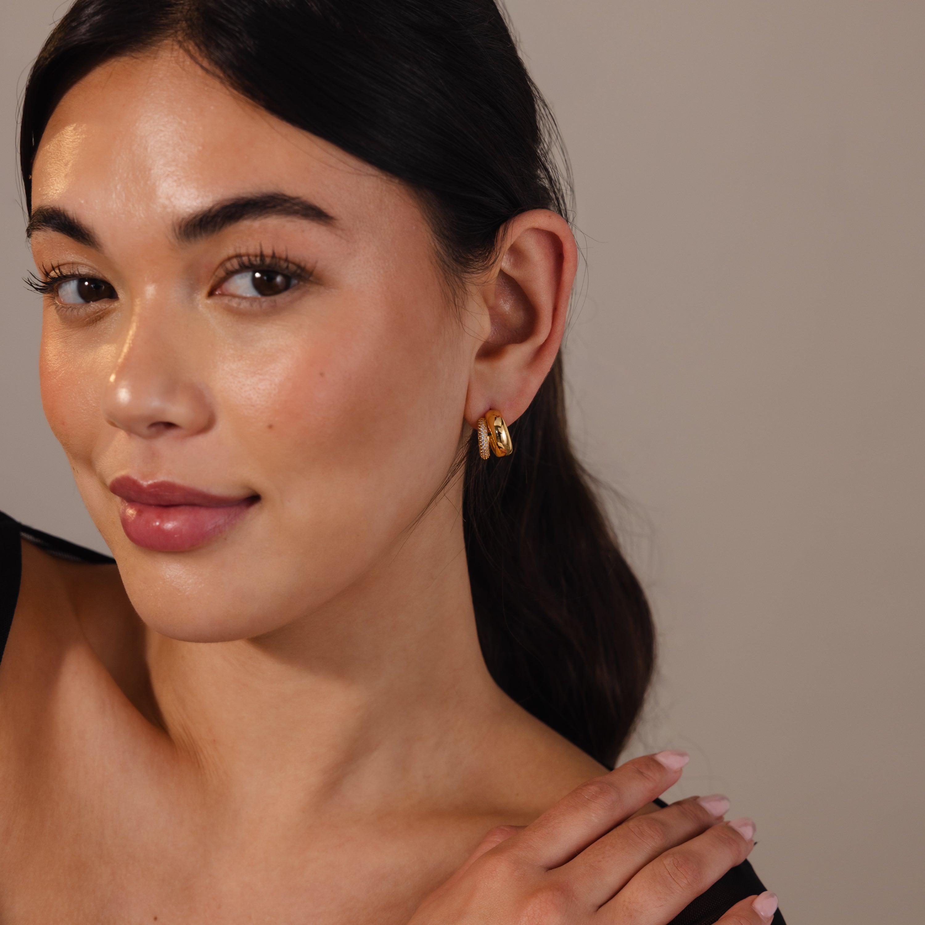 Woman with long dark hair wears Duo Pave Dome Studs in 18K Gold, smiling softly against a neutral background—a simple, effortless showcase of everyday jewelry.