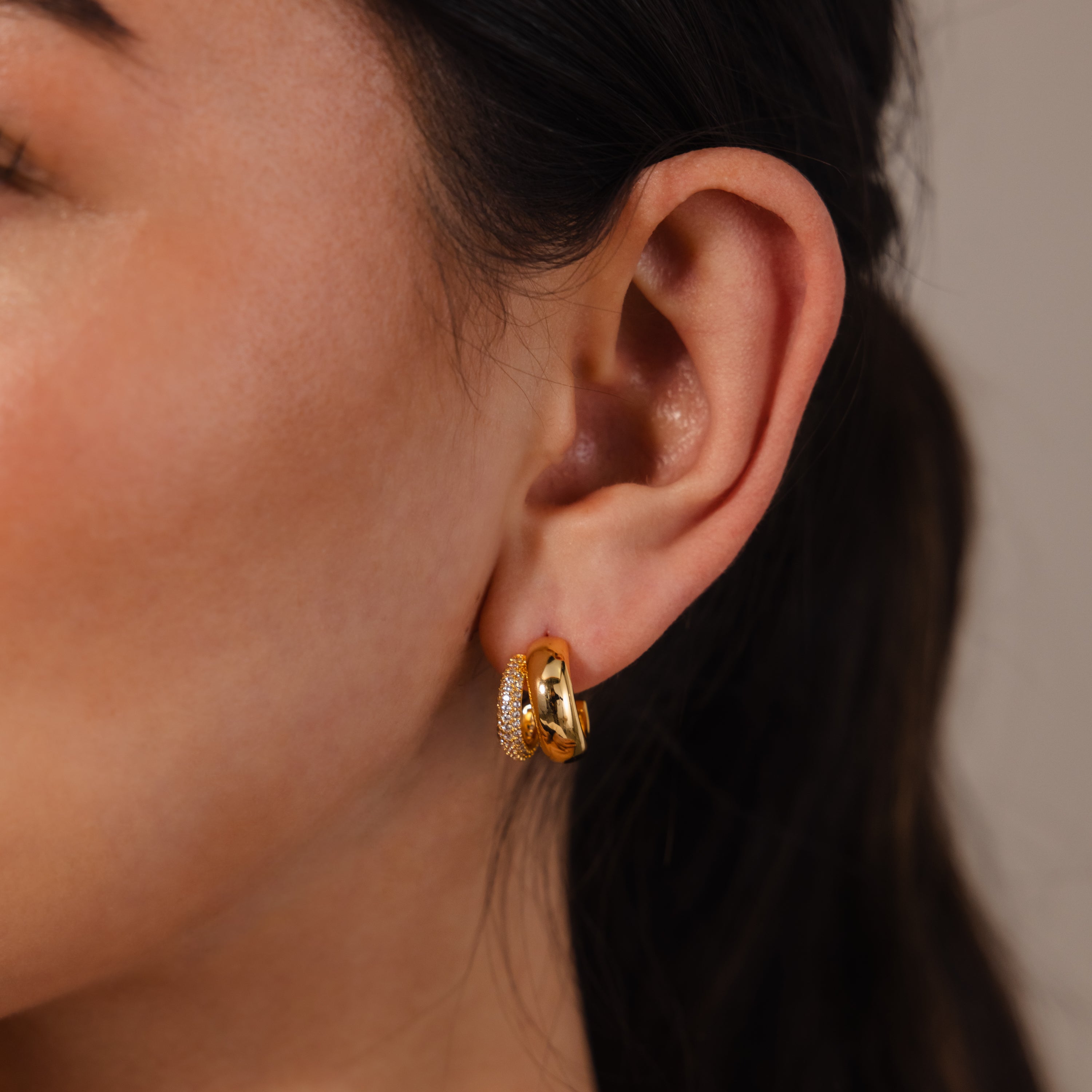 Close-up of a woman’s ear wearing two gold hoop earrings—one plain, one with clear stones—styled with the Duo Pave Dome Studs in Mixed Metal for a chic pavé accent, perfect for elevating your everyday jewelry look.