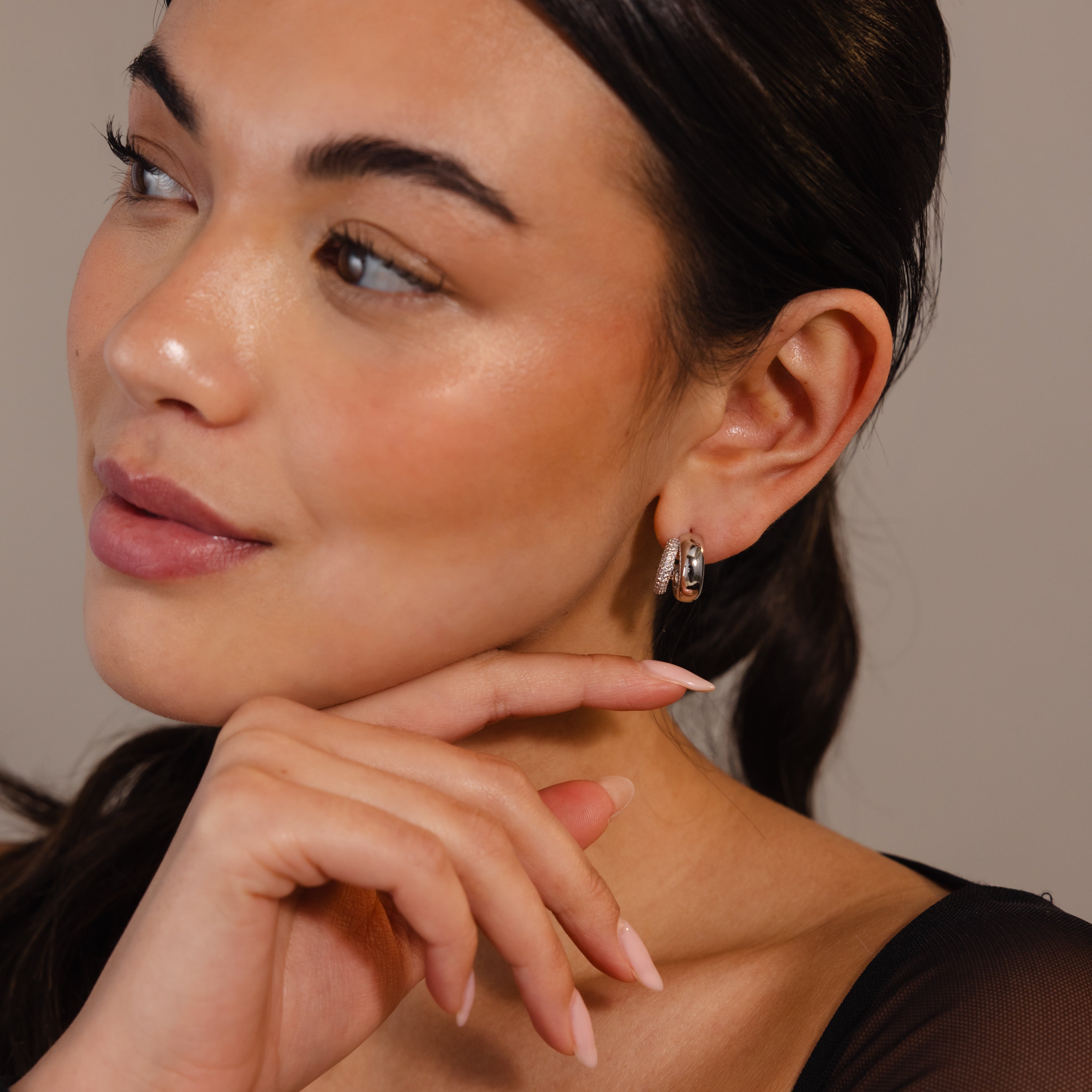Woman with smooth skin and glossy lips wears Duo Pave Dome Studs in Mixed Metal—an effortless touch of everyday jewelry—while touching her face with a manicured hand.