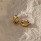 The Duo Pave Dome Studs in 18K Gold rest on crumpled, light-colored paper—a stunning pair of earrings perfect for everyday jewelry lovers.