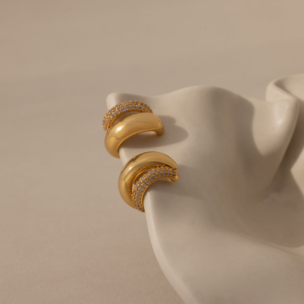 Duo Pave Dome Studs in 18K Gold, adorned with crystal pavé, rest on a wavy white ceramic dish against a beige backdrop—an elegant choice to elevate your everyday jewelry collection.