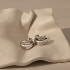 The Duo Pave Dome Studs—silver earrings with diamond pavé—are displayed on a wavy, cream ceramic dish, adding elegance to your everyday jewelry collection.