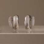 Duo Pave Dome Studs in White Gold, featuring one earring encrusted with clear pavé stones, are displayed on a clear surface—perfect as standout everyday jewelry.