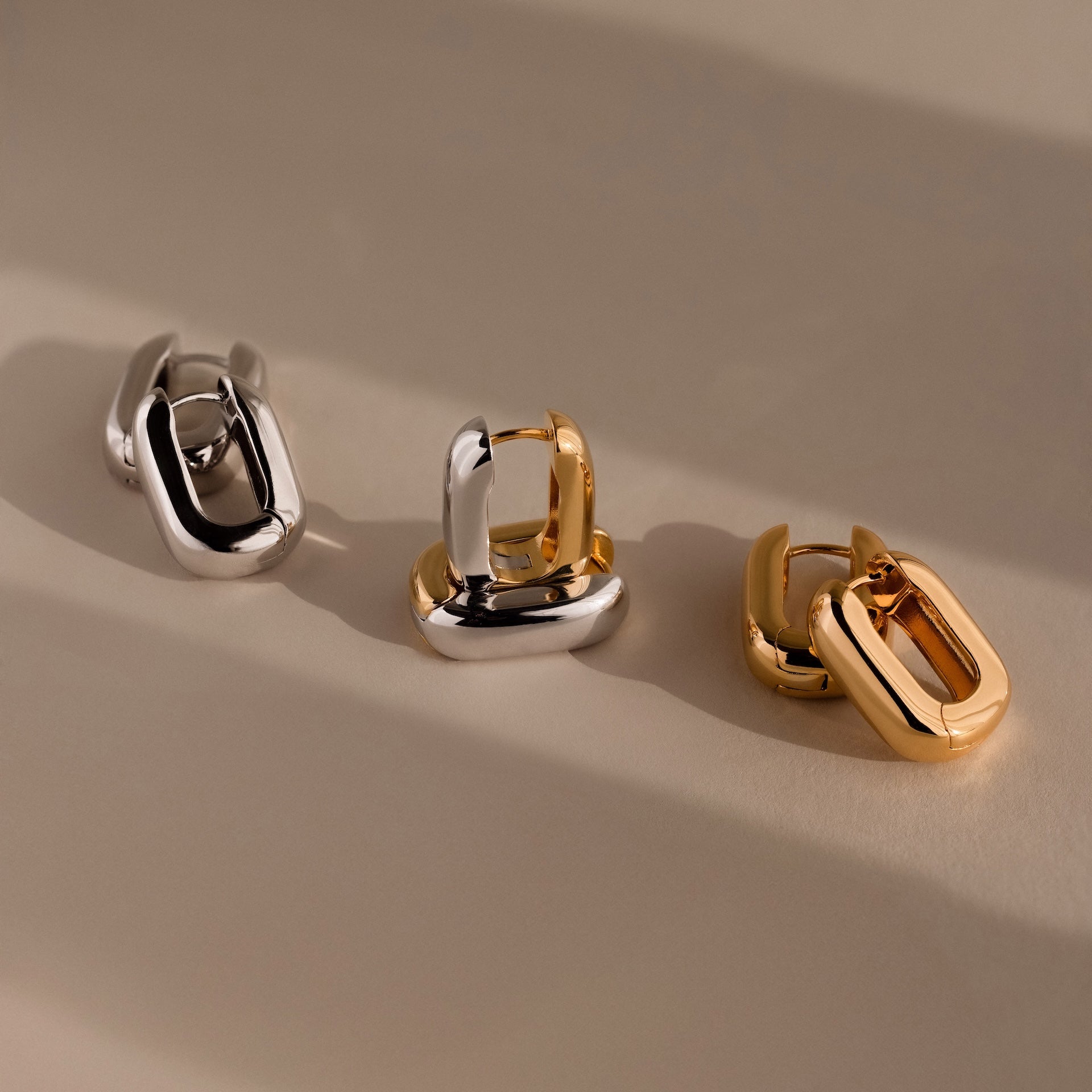 Bold Link Hoops are showcased in three chunky, interlocking designs—silver, mixed silver-gold, and gold—highlighting their modern style against a neutral background.