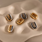 The Bold Link Hoops, along with four other gold and silver oval hoop earrings—some chunky—are displayed on a wavy, beige ceramic dish.