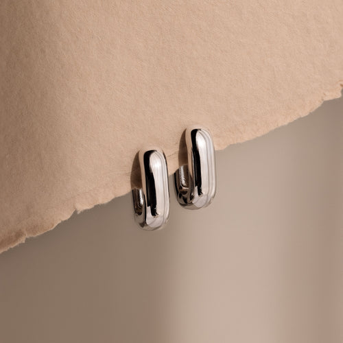 Bold Link Hoops in White Gold rest on a textured beige surface under soft lighting, highlighting the modern elegance of this jewelry piece.