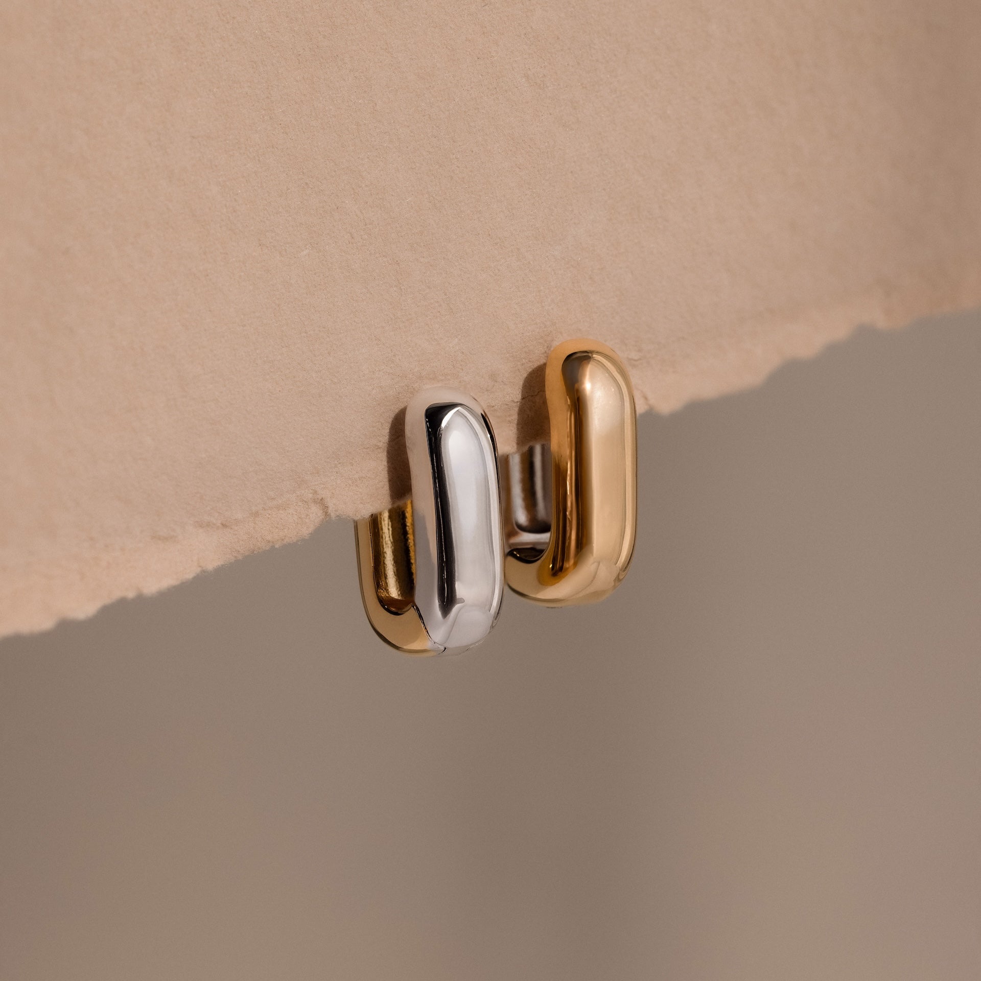 Two Bold Link Hoops in Mixed Metal—one silver, one gold—rest on beige textured paper. These chunky earrings add a modern, striking touch, ideal for anyone who loves bold link and chunky hoop styles.