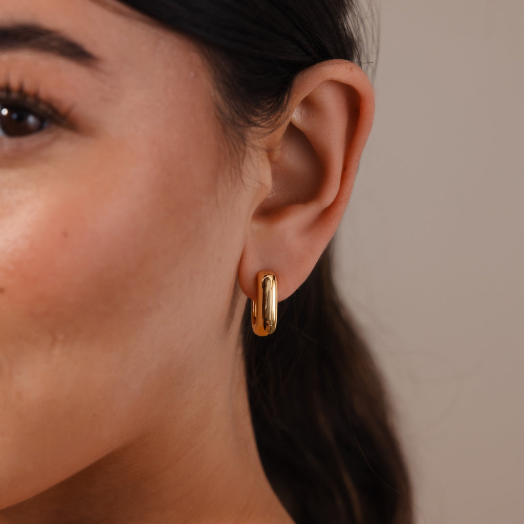 A close-up of a woman's ear wearing Bold Link Hoops—a pair of modern, gold hoop earrings.