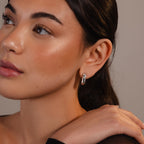 A woman with smooth skin and dark hair wears the Bold Link Hoops in White Gold, gazing thoughtfully to the side—a striking example of modern jewelry.