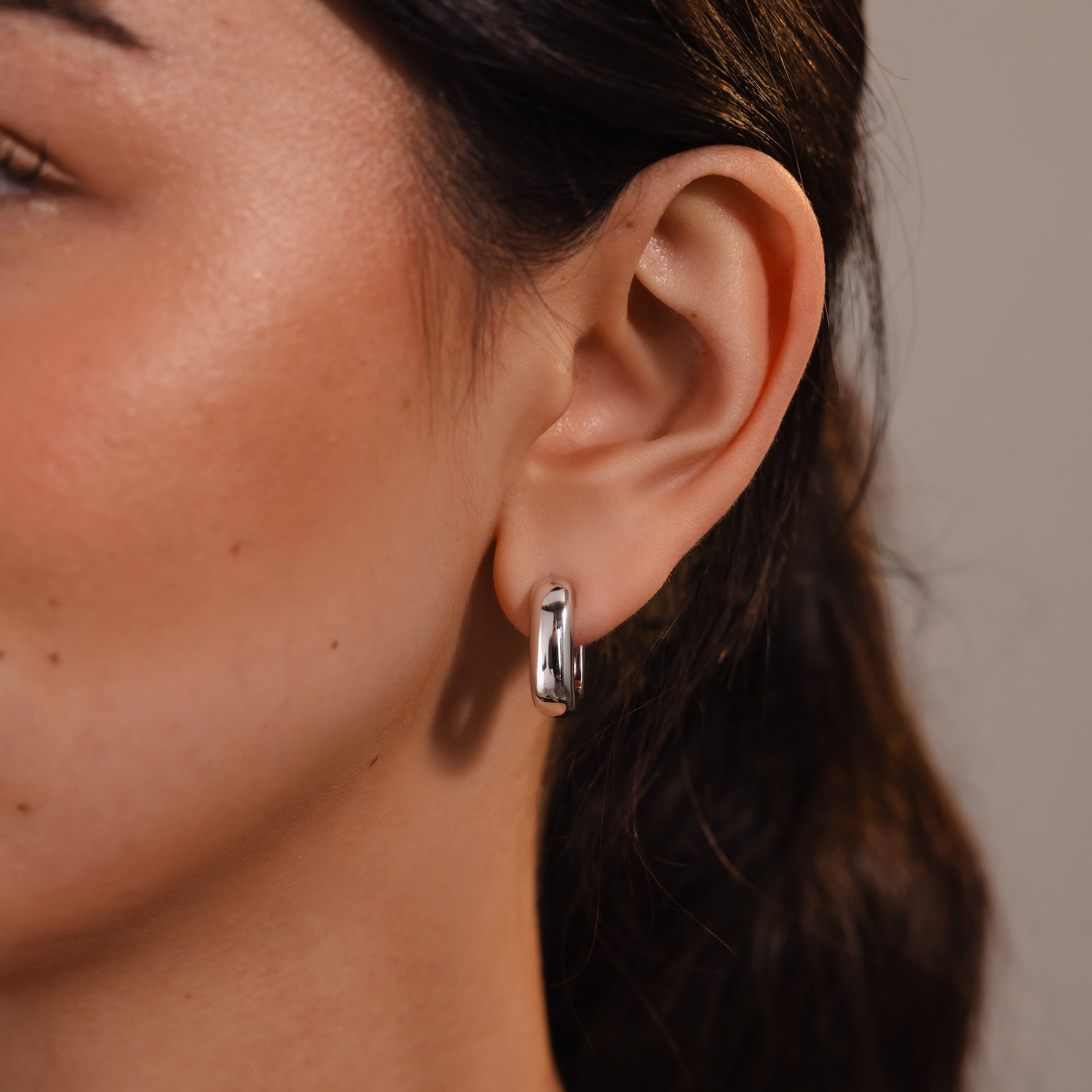 Close-up of a woman’s ear wearing Bold Link Hoops in White Gold, highlighting modern jewelry style against her long brown hair.