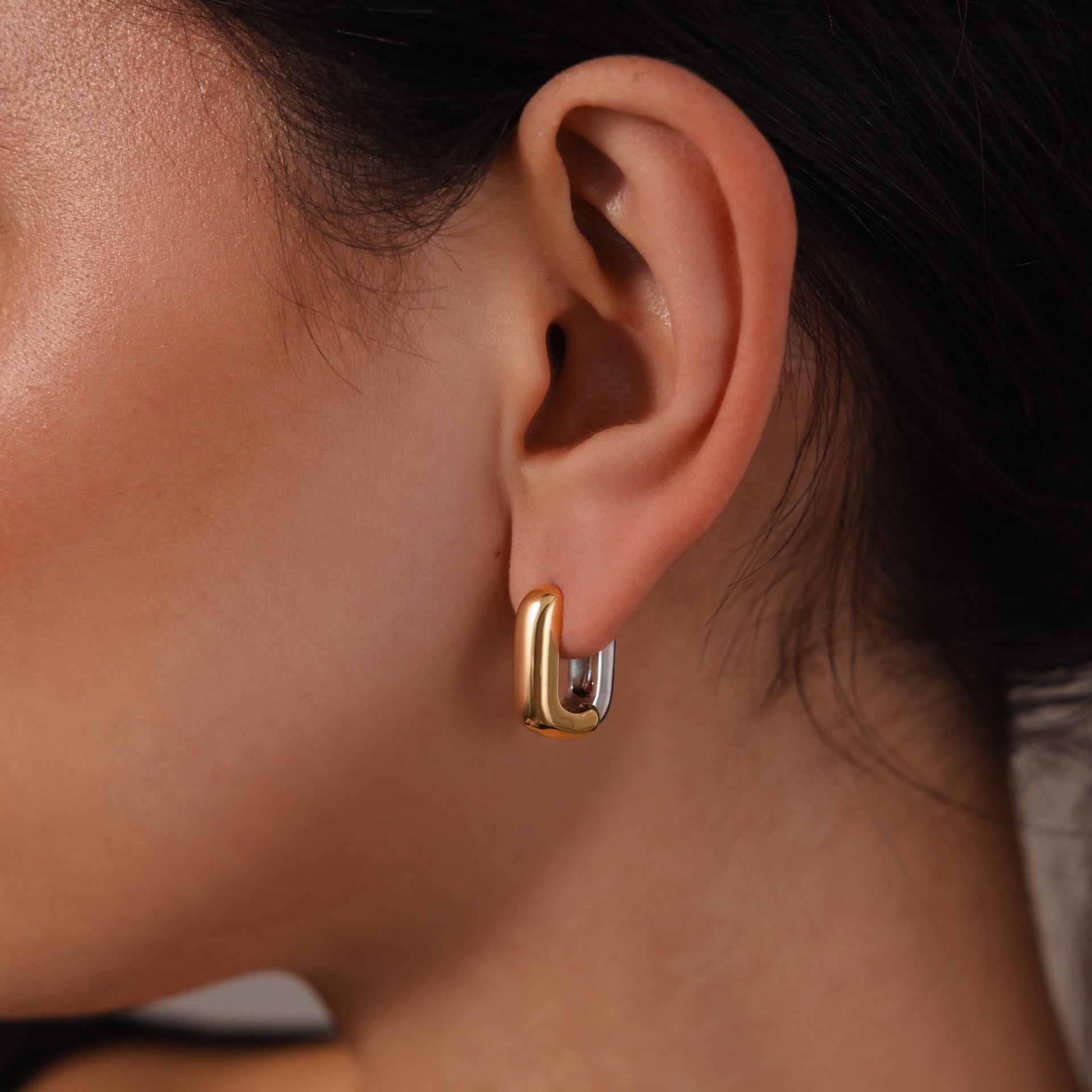 A close-up of a woman's ear showcases the Bold Link Hoops in Mixed Metal—modern gold and silver chunky hoops that add a striking touch to her look.