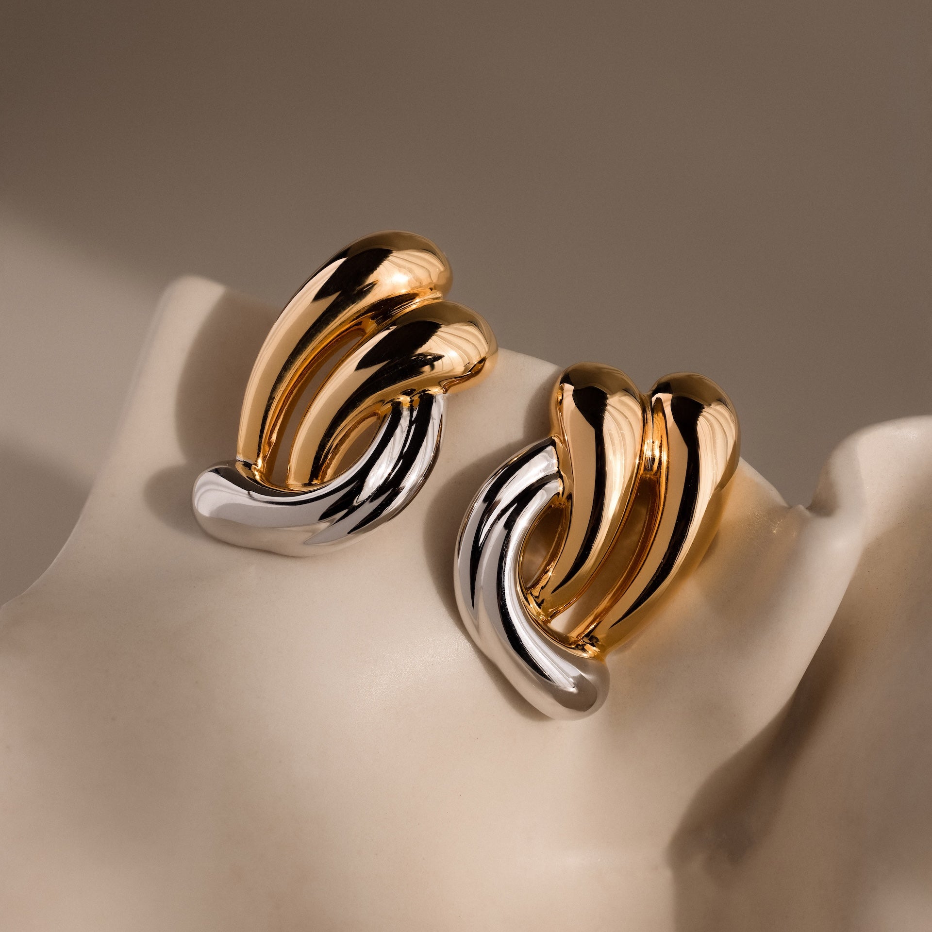 The Mixed Metal Raindrop Studs are elegant gold and silver earrings, shown on a light mannequin ear under soft lighting.