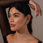 Woman with long dark hair poses in a sheer black top and raises her hand over her head, showcasing Mixed Metal Raindrop Studs—sculptural gold and silver earrings.