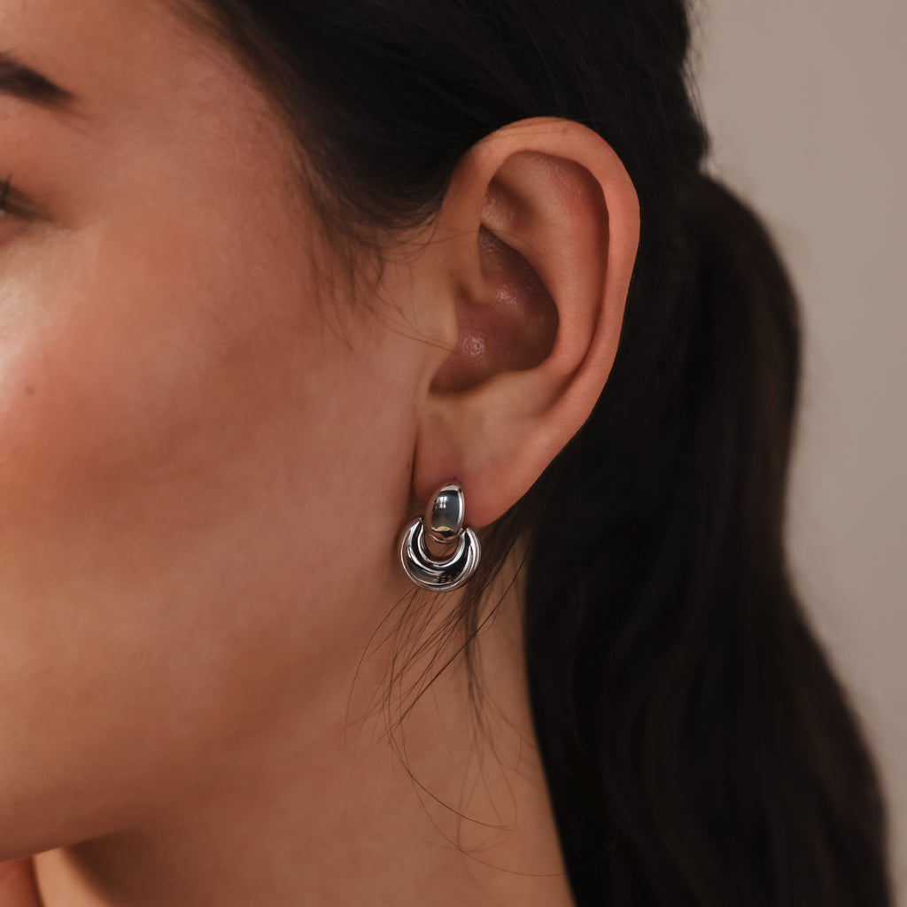 A close-up of a woman's ear adorned with Eclipse Dome Studs in White Gold, showcasing sculptural earrings that embody modern jewelry design.