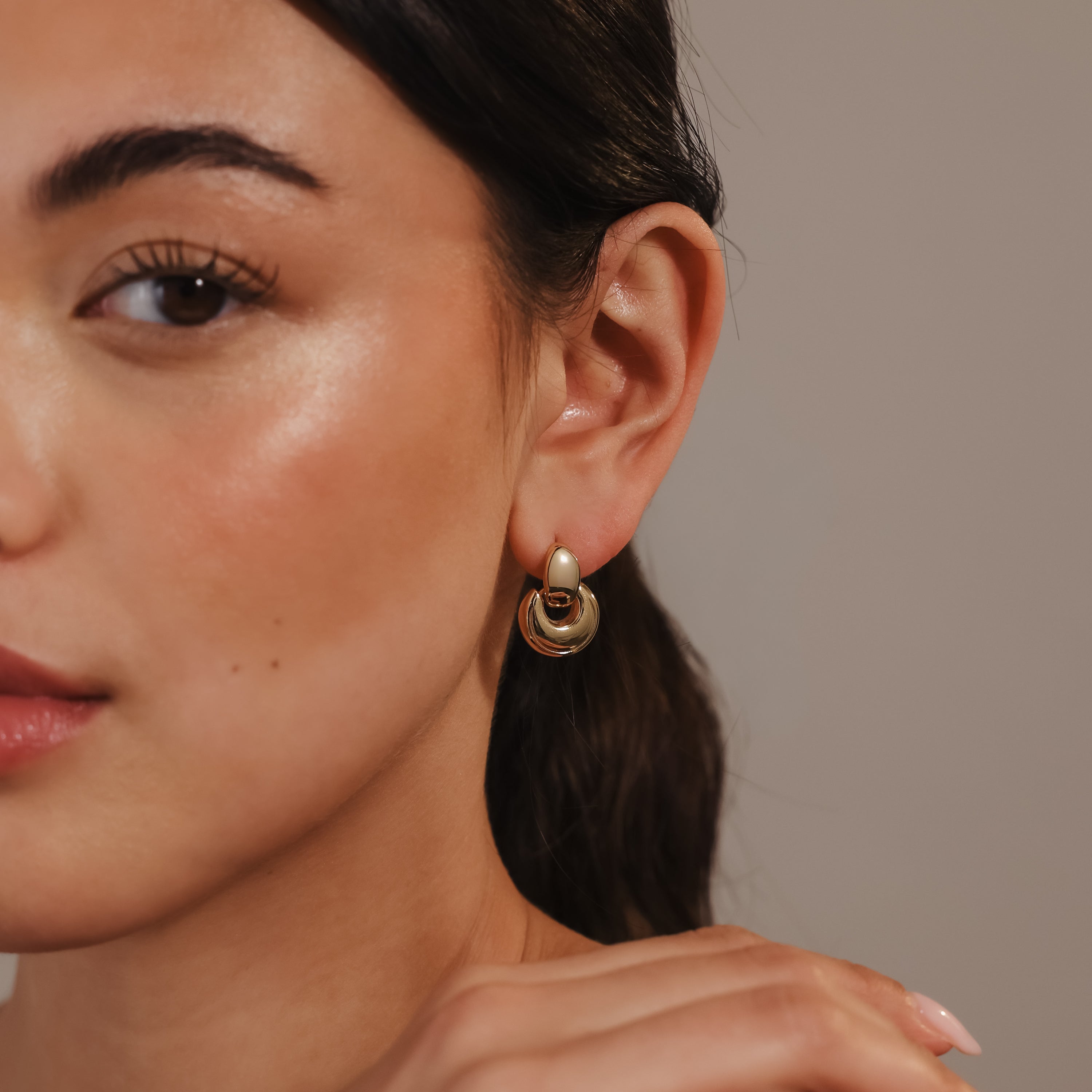 A woman with glowing skin wears the Eclipse Dome Studs—modern, sculptural earrings—shown from the side against a neutral background.