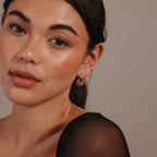 Woman with smooth skin and dark hair wears the Eclipse Dome Studs in 18K gold—sculptural earrings—paired with a black sheer top, facing the camera.