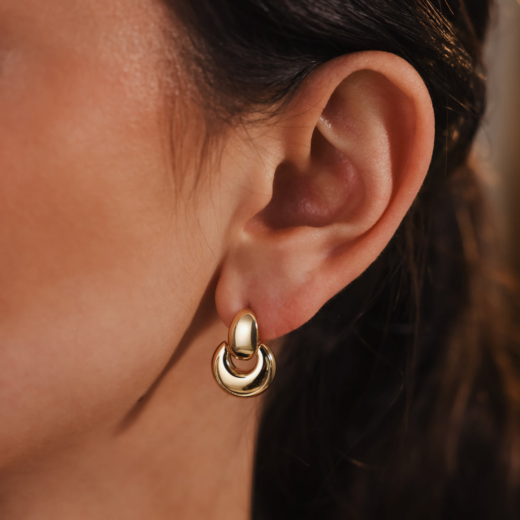 Close-up of a woman's ear wearing Eclipse Dome Studs in 18K Gold, highlighting the modern elegance and shiny finish of these contemporary stud earrings.