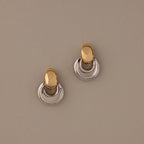 The Eclipse Dome Studs in Mixed Metal feature oval tops and curved half-moon bottoms, highlighting sculptural design against a beige background.