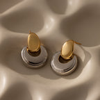 The Eclipse Dome Studs in Mixed Metal, featuring gold and silver crescent shapes, rest on a cream wavy textured surface, highlighting the elegance of modern jewelry design.