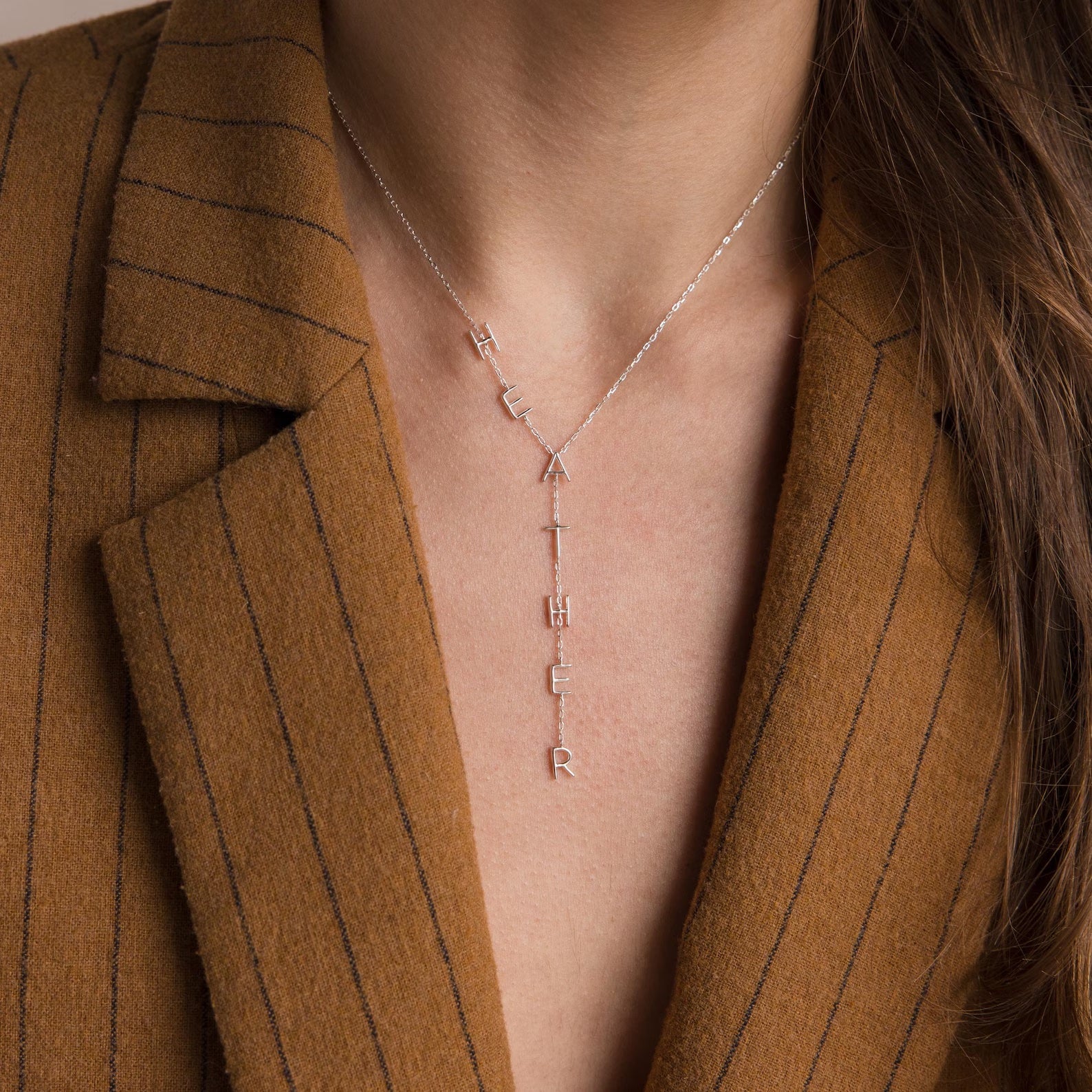 A woman wearing a brown pinstripe blazer and a Lariat Name Necklace.