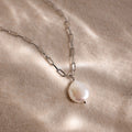 Silver link chain pearl pendant necklace on a beige sandy textured surface
