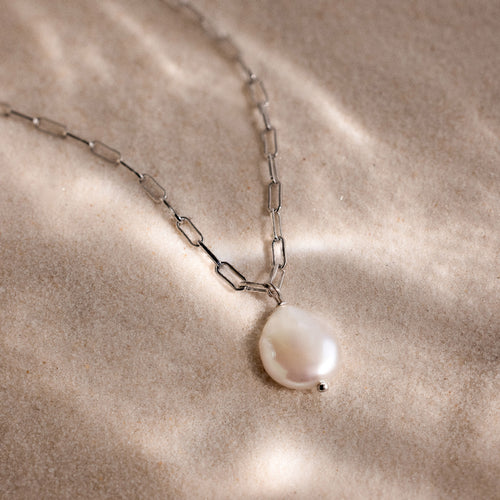 Silver link chain pearl pendant necklace on a beige sandy textured surface