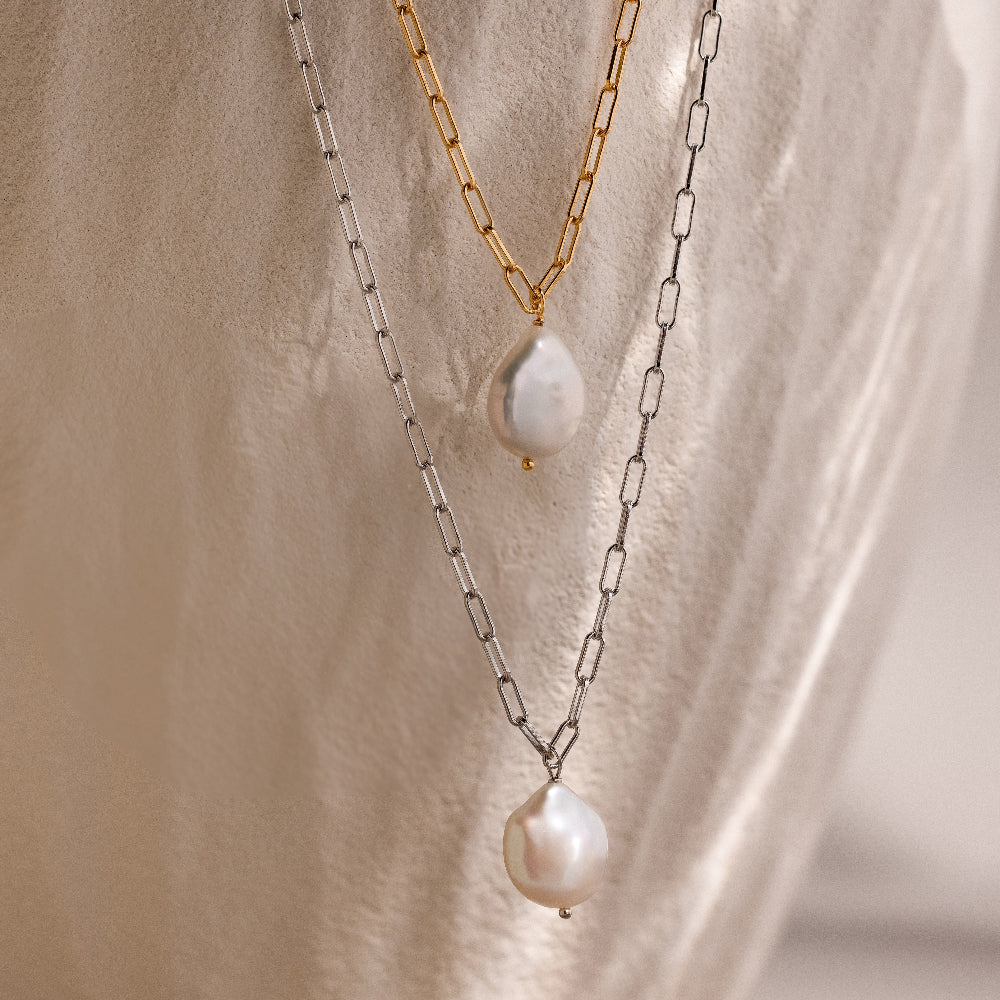 Two link chain pearl necklaces in gold and silver on a beige stone background